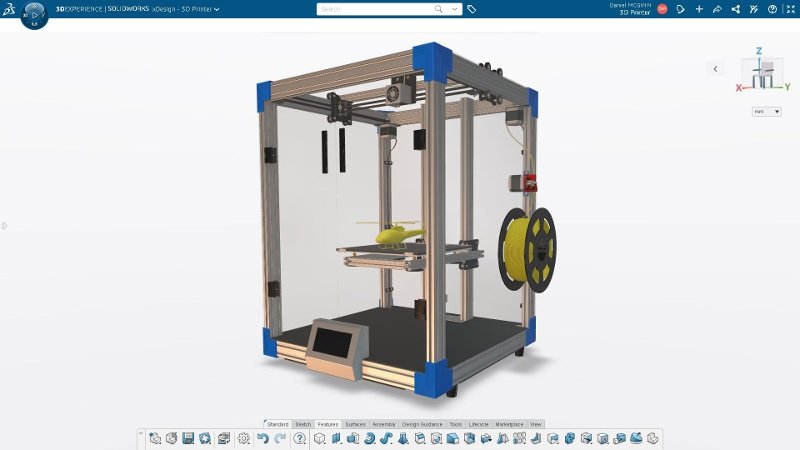 A imagem é um print de tela de software, com o aplicativo xDesign aberto no ambiente da Plataforma 3DEXPERIENCE, pronto para impressão 3D de uma forma complexa. Ao centro da imagem, há uma espécie de caixa com um pequeno helicóptero centralizado - é a peça que deve ser fabricada em 3D.